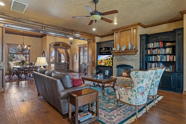 living room with a warm lit fireplace, ceiling fan with notable chandelier, dark wood-style flooring, visible vents, and crown molding