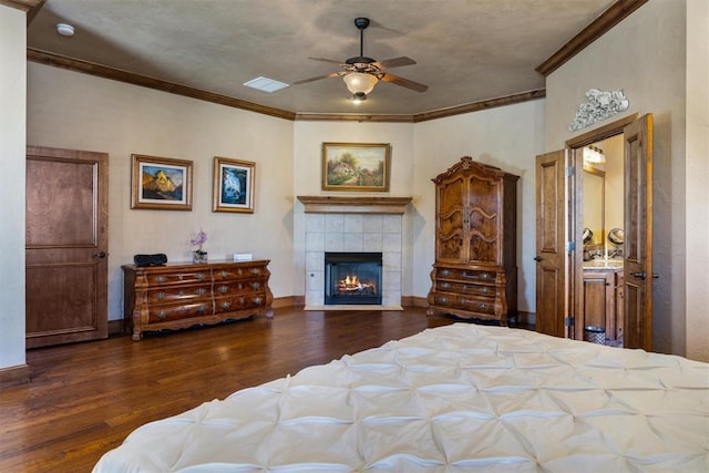 bedroom featuring baseboards, visible vents, a tiled fireplace, wood finished floors, and crown molding