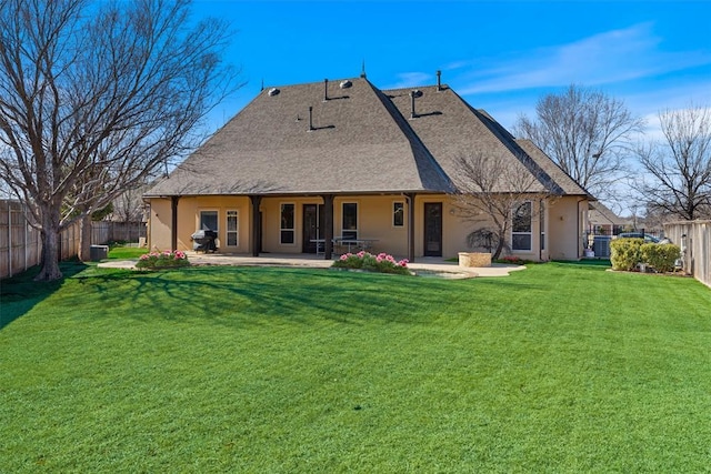 rear view of property featuring a fenced backyard, a shingled roof, a lawn, stucco siding, and a patio area