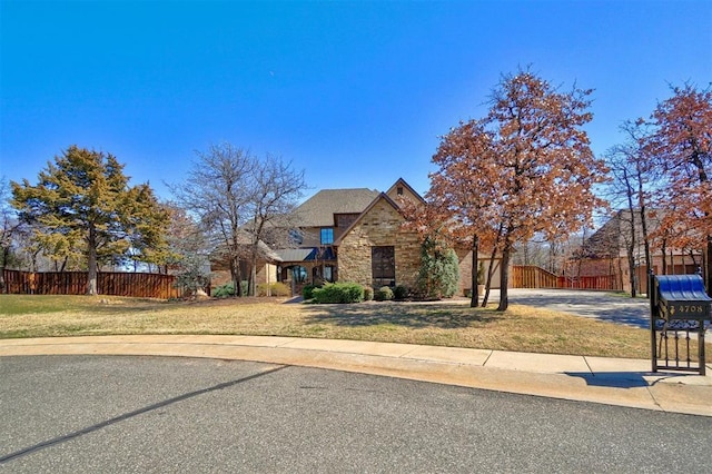 view of front of house with stone siding, fence, and a front lawn