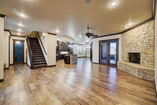 unfurnished living room featuring a fireplace, stairs, french doors, light wood-type flooring, and crown molding