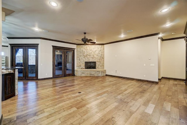 unfurnished living room with ceiling fan, a stone fireplace, french doors, and light wood-style floors