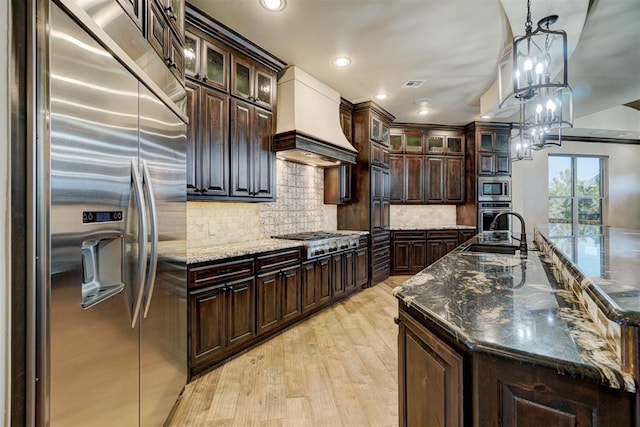 kitchen featuring built in appliances, premium range hood, visible vents, light wood-style floors, and backsplash