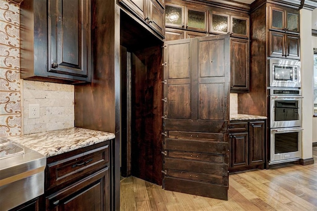 kitchen with dark brown cabinetry, light wood-style flooring, decorative backsplash, and stainless steel appliances