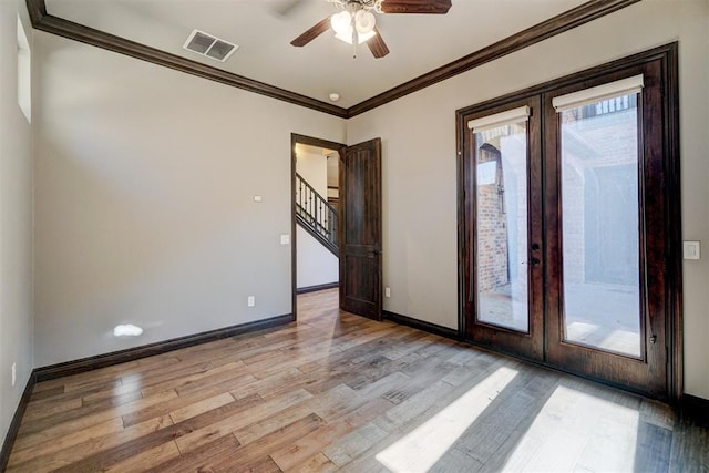 empty room featuring light wood-style flooring, visible vents, baseboards, ornamental molding, and french doors