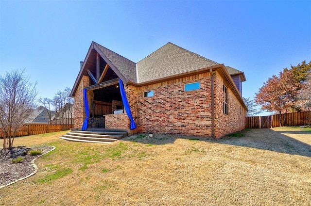 view of front of property with a front yard, brick siding, a fenced backyard, and roof with shingles