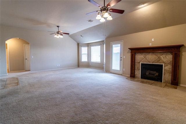 unfurnished living room featuring light carpet, visible vents, arched walkways, a tiled fireplace, and vaulted ceiling