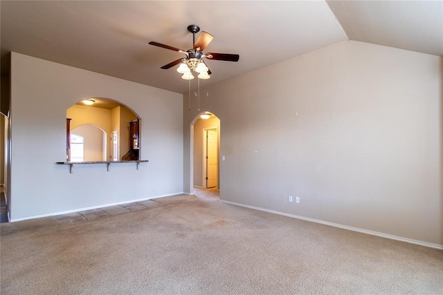 spare room with arched walkways, a ceiling fan, light carpet, vaulted ceiling, and baseboards