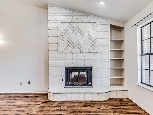 room details featuring a brick fireplace, built in shelves, baseboards, and wood finished floors