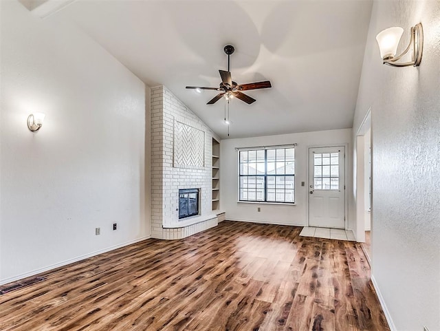 unfurnished living room with built in shelves, a ceiling fan, a brick fireplace, vaulted ceiling, and wood finished floors