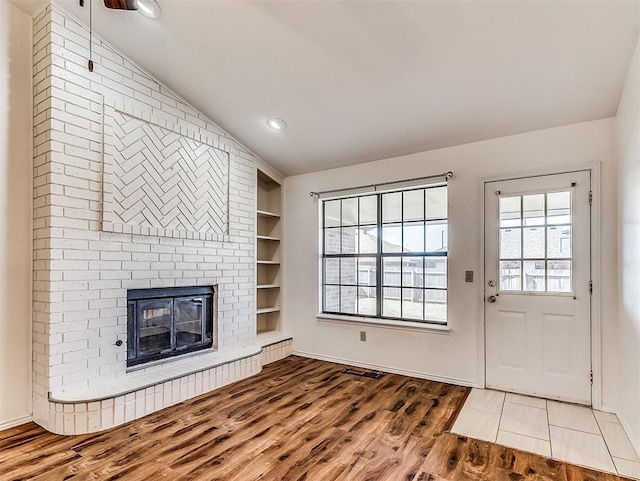 unfurnished living room featuring lofted ceiling, built in shelves, wood finished floors, baseboards, and a brick fireplace