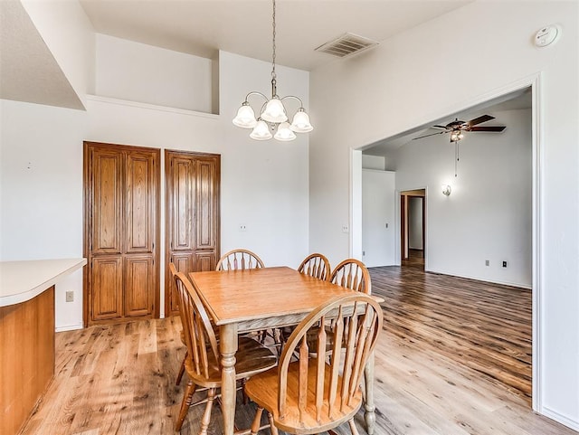 dining room featuring ceiling fan with notable chandelier, high vaulted ceiling, light wood finished floors, and visible vents