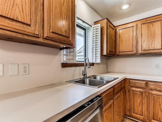 kitchen with light countertops, brown cabinetry, a sink, and dishwashing machine