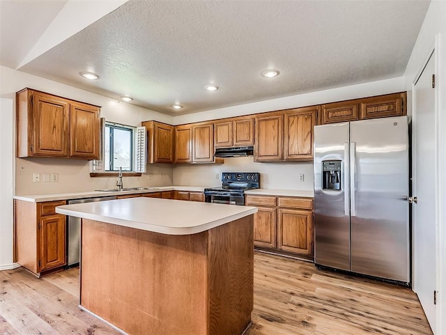 kitchen featuring brown cabinets, under cabinet range hood, stainless steel appliances, and a sink