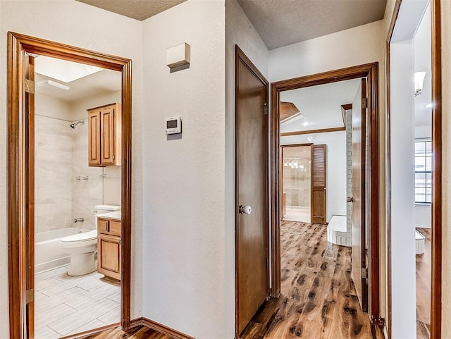 hallway featuring light wood-type flooring, a textured ceiling, and a textured wall