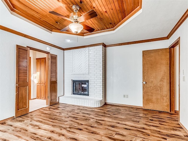 unfurnished living room featuring wood finished floors, wood ceiling, ornamental molding, a brick fireplace, and a tray ceiling