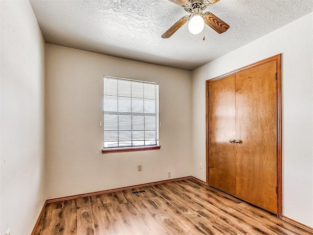 unfurnished bedroom with a closet, visible vents, light wood-style floors, ceiling fan, and a textured ceiling