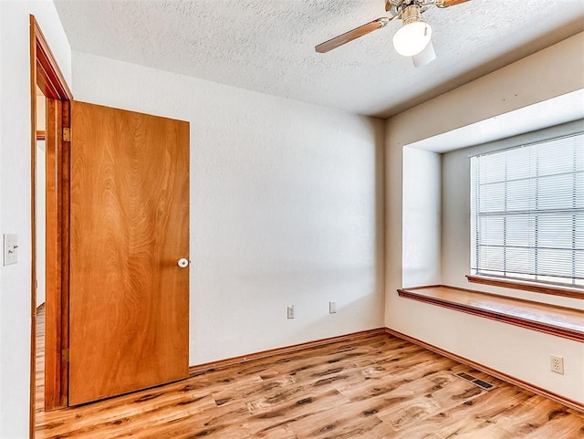 spare room featuring light wood-style floors, visible vents, ceiling fan, and a textured ceiling