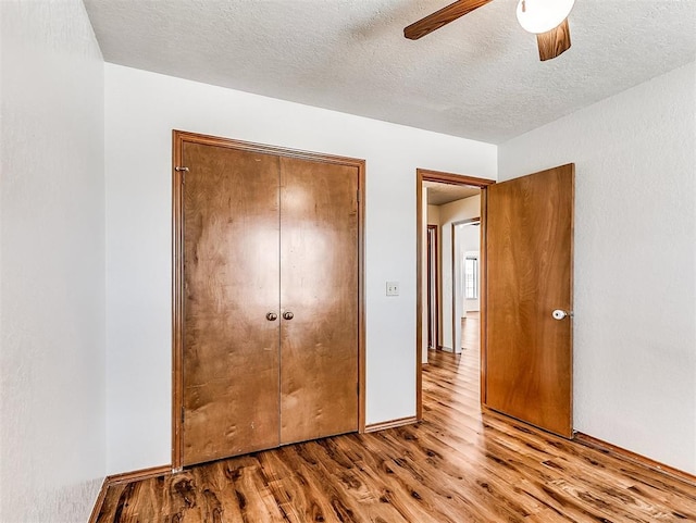 unfurnished bedroom featuring a textured ceiling, wood finished floors, a ceiling fan, baseboards, and a closet