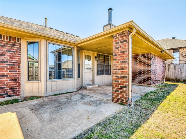 doorway to property with a chimney, fence, a patio area, board and batten siding, and brick siding