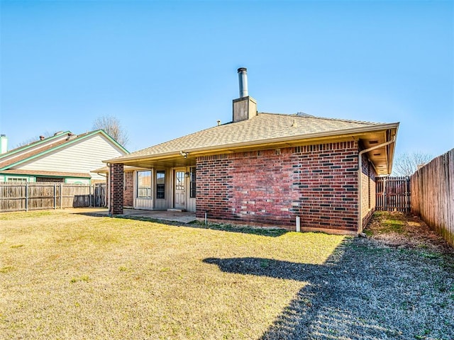 rear view of property featuring a yard, brick siding, a chimney, and a fenced backyard