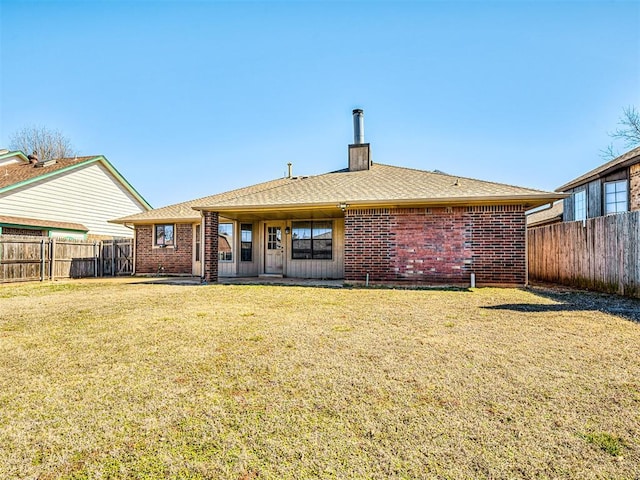 rear view of house featuring a yard, a fenced backyard, a chimney, and brick siding