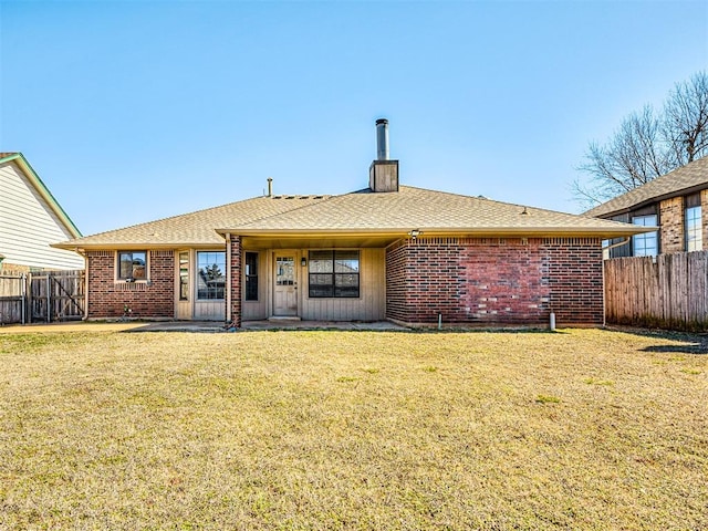 rear view of property with brick siding, a shingled roof, fence, a yard, and a chimney