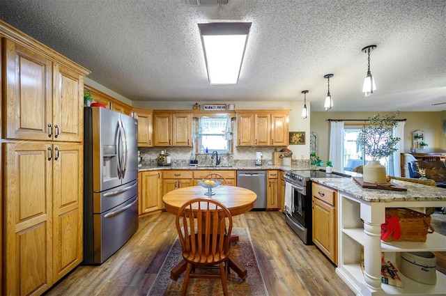 kitchen with light wood-style flooring, a peninsula, a sink, stainless steel appliances, and backsplash