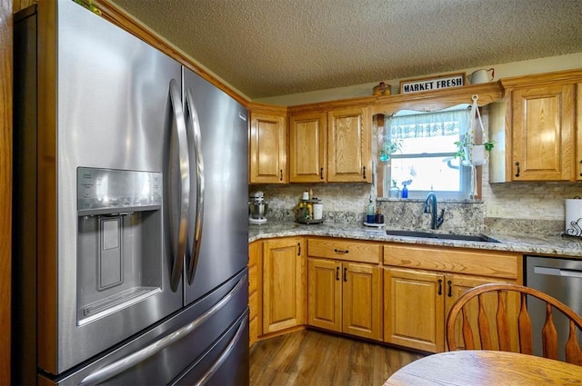 kitchen with tasteful backsplash, light stone counters, dark wood-type flooring, stainless steel appliances, and a sink