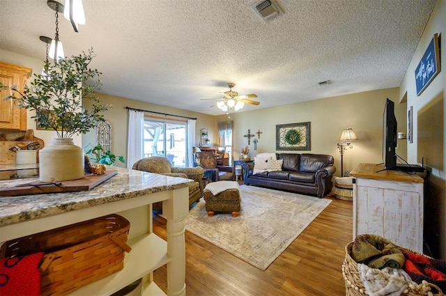 living room featuring ceiling fan, a textured ceiling, wood finished floors, and visible vents