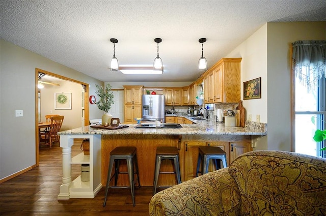 kitchen featuring stainless steel fridge with ice dispenser, dark wood-type flooring, a peninsula, light stone countertops, and a sink