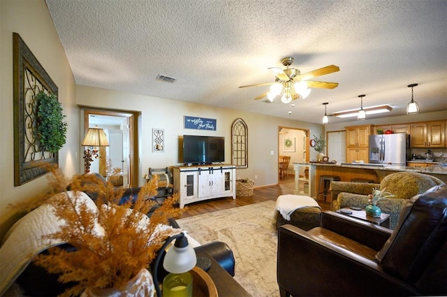 living room with ceiling fan, a textured ceiling, wood finished floors, and visible vents