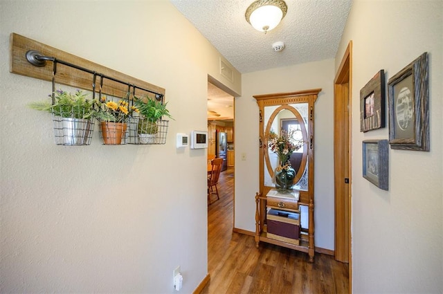 corridor with a textured ceiling, wood finished floors, and baseboards