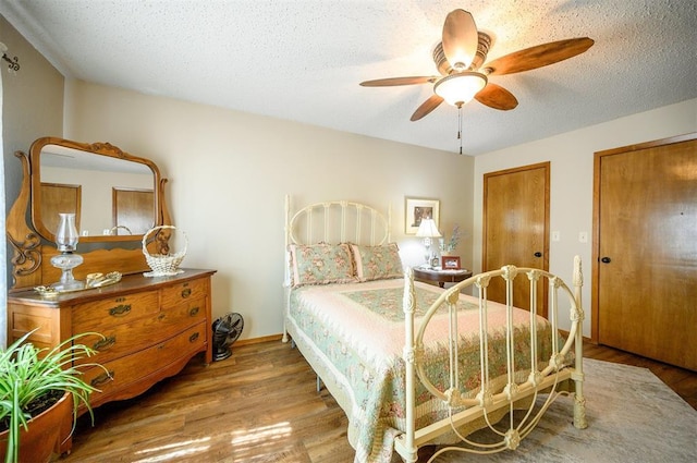 bedroom with baseboards, a ceiling fan, wood finished floors, a textured ceiling, and multiple closets