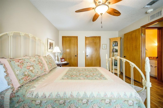 bedroom featuring a textured ceiling, visible vents, two closets, and wood finished floors