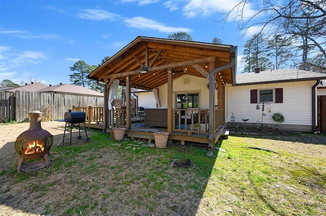 rear view of property with a fire pit, fence, a deck, and a lawn