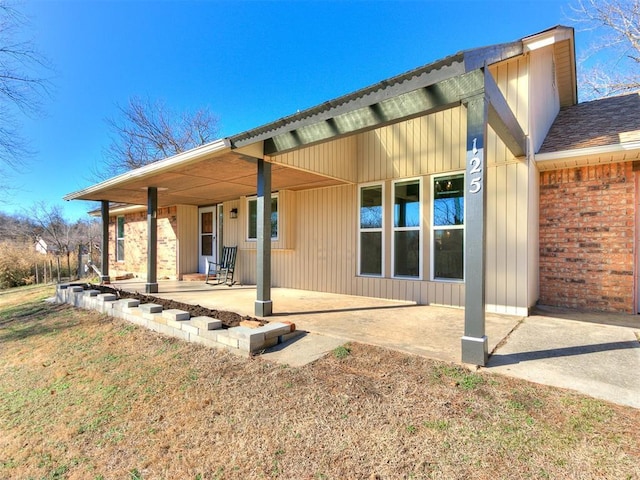 back of property featuring a shingled roof, a patio, and brick siding