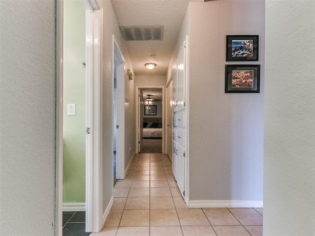 corridor featuring light tile patterned floors, baseboards, visible vents, a textured wall, and a textured ceiling