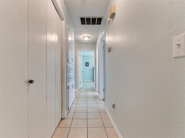 corridor with light tile patterned floors, visible vents, a textured wall, a textured ceiling, and baseboards