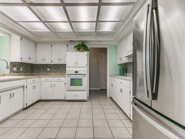 kitchen with white oven, freestanding refrigerator, white cabinets, a sink, and under cabinet range hood