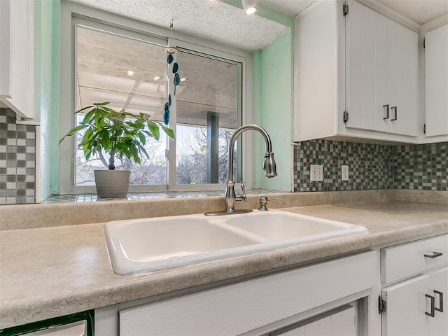 kitchen with tasteful backsplash, light countertops, white cabinets, and a sink