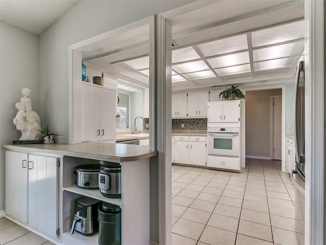 kitchen featuring white oven, light tile patterned floors, tasteful backsplash, open shelves, and white cabinetry