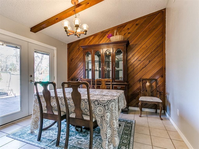 dining area with a textured ceiling, light tile patterned floors, wood walls, beam ceiling, and an inviting chandelier