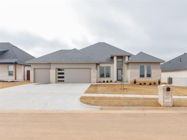 prairie-style house featuring driveway, brick siding, roof with shingles, and an attached garage