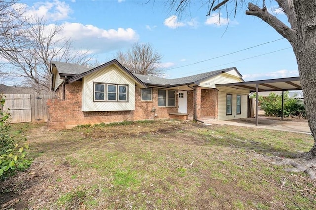 view of front facade with brick siding, concrete driveway, a front yard, fence, and an attached carport