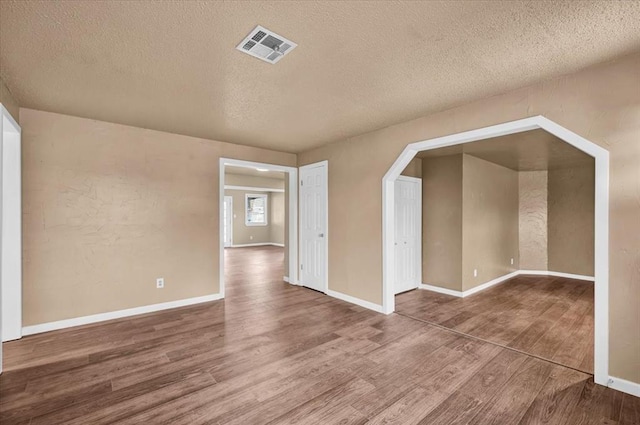 interior space featuring baseboards, a textured ceiling, visible vents, and wood finished floors