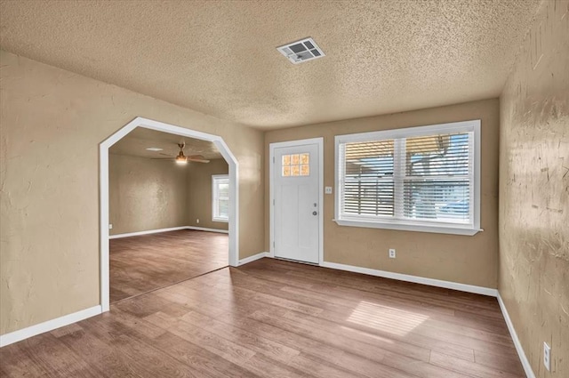 entrance foyer featuring arched walkways, visible vents, a textured wall, and wood finished floors