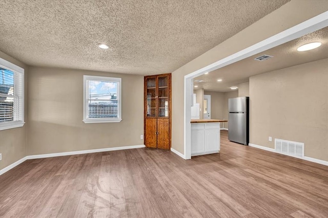 spare room featuring light wood-type flooring, baseboards, visible vents, and a textured ceiling