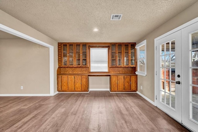 unfurnished room with a wealth of natural light, built in desk, wood finished floors, and visible vents