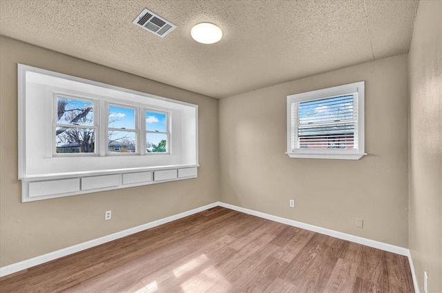 unfurnished room with baseboards, a textured ceiling, visible vents, and wood finished floors